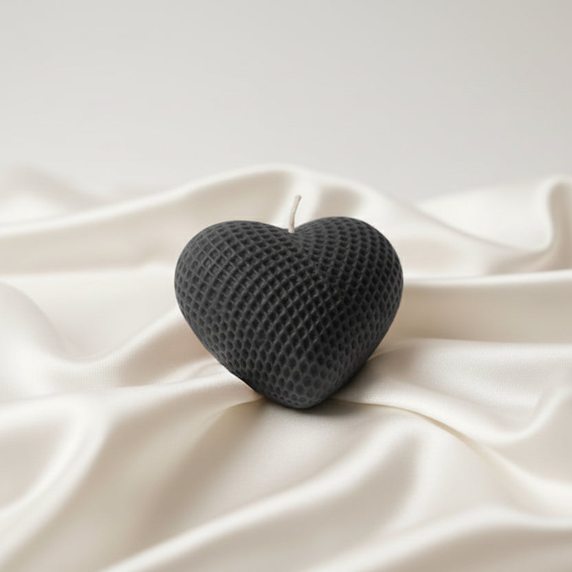Black textured heart-shaped candle on a white fabric background