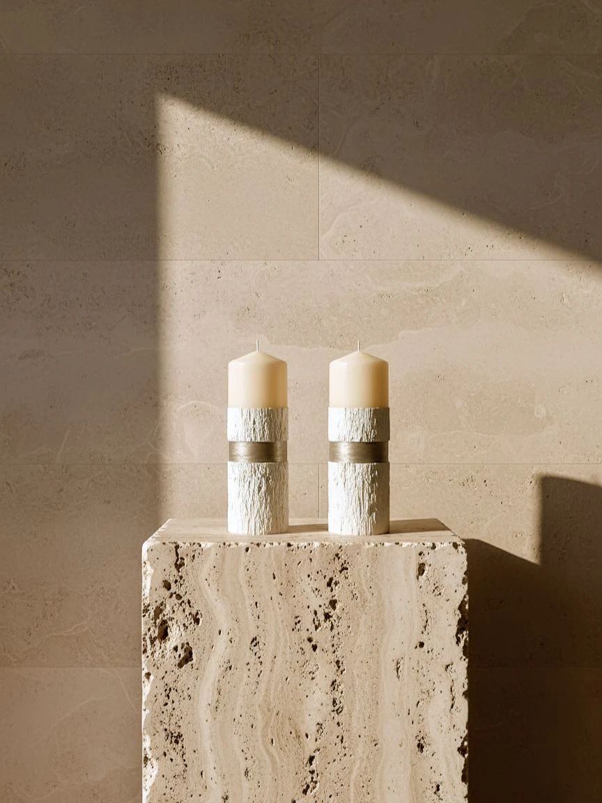 A pale wax pillar banded in soft metallic light, resting on grey concrete